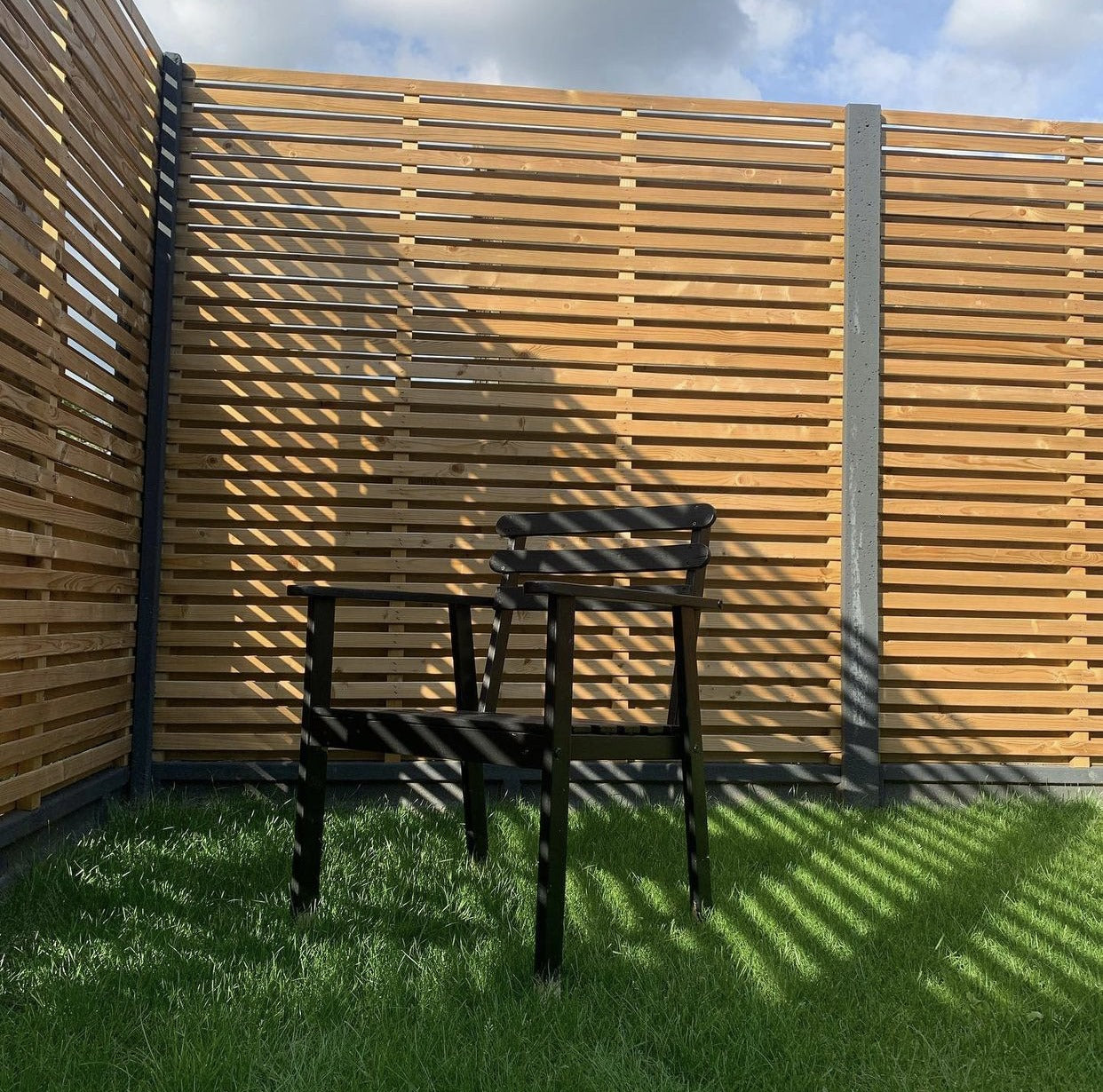 Beautifully fitted double slatted fence installation, with black posts and black garden chair