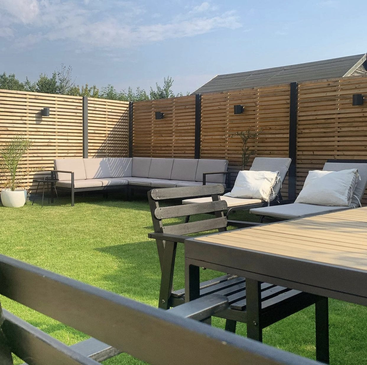 Beautifully fitted double slatted fence installation, with black posts. Slick corner garden sofa in cream with two single cream loungers